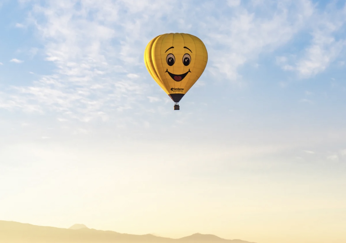 ballon dirigeable jaune avec une tete de smiley dans un ciel bleu au dessus du desert